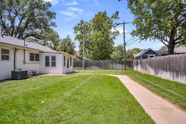 Spacious backyard with a concrete path, manicured lawn, and wooden fence under a clear blue sky.