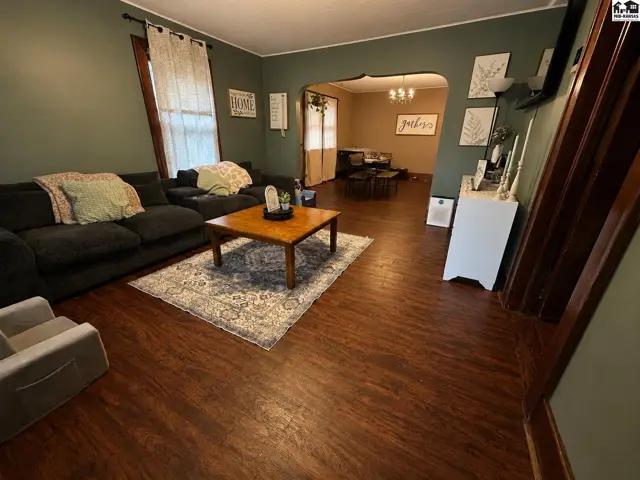 Cozy living room with dark green walls, dark wood floors, a large sectional, and a wooden coffee table.