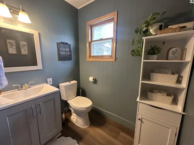 A bathroom with teal paneled walls, a gray vanity, white sink, and a tall white storage cabinet.