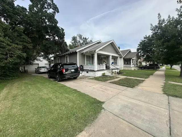 Gray bungalow with white trim, porch, and mature trees sits on a tree-lined street.