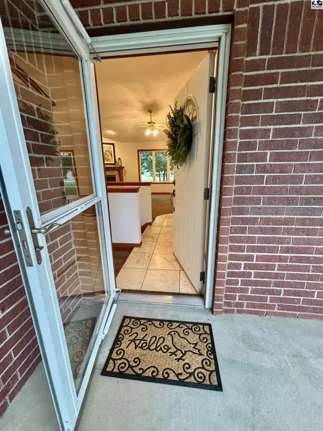Brick exterior with an open screen door revealing a tiled entryway and living area.