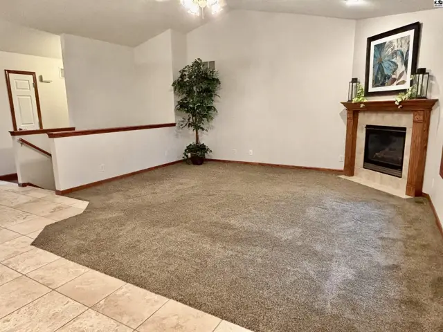 Spacious living room with plush carpet, a gas fireplace, and a wooden mantel.
