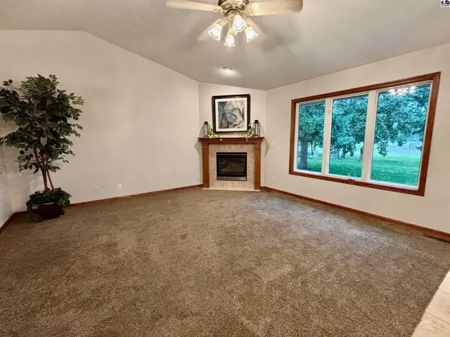 Spacious living room with a corner gas fireplace, large window, and plush carpet.