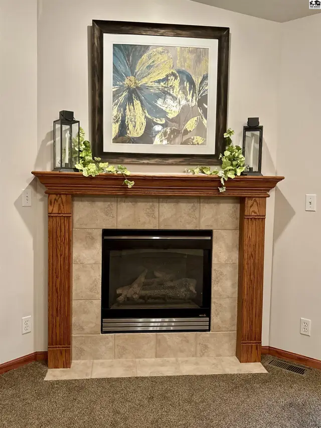 A traditional fireplace features a tiled surround, oak mantel, and framed floral artwork.