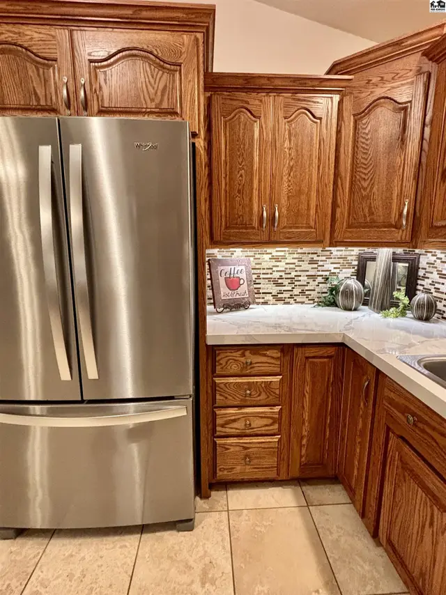 Kitchen corner with stainless steel refrigerator, oak cabinets, and a decorative backsplash.