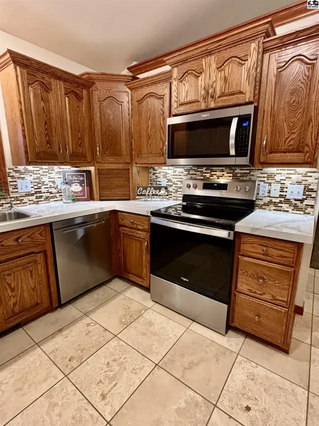 Kitchen with warm oak cabinets, stainless steel appliances, and a mosaic tile backsplash.