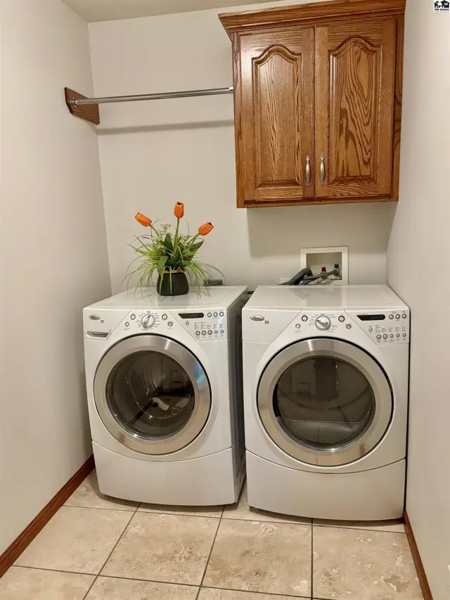 Laundry room with white front-load washer and dryer, tiled floor, and oak cabinetry.
