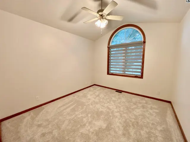 Empty bedroom with vaulted ceiling, fan, and arched window with blinds.