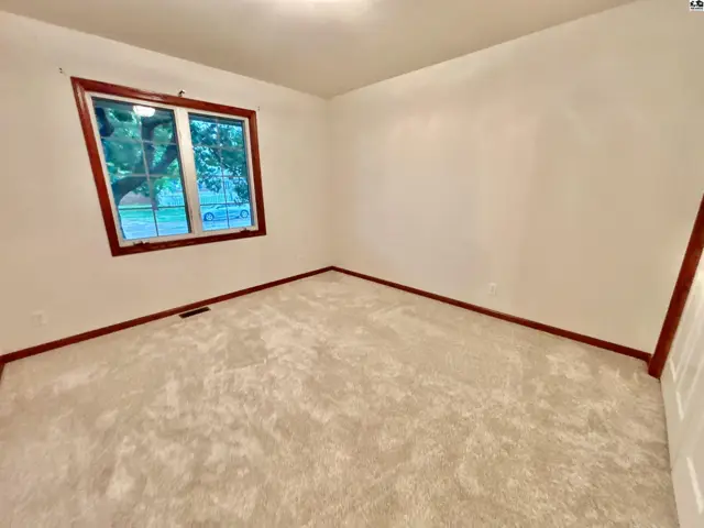 Empty bedroom with plush carpet, white walls, and a wood-trimmed window overlooking trees.