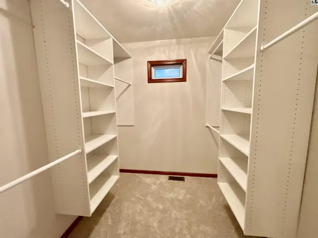 Spacious walk-in closet with white shelving, carpet, and a small window.
