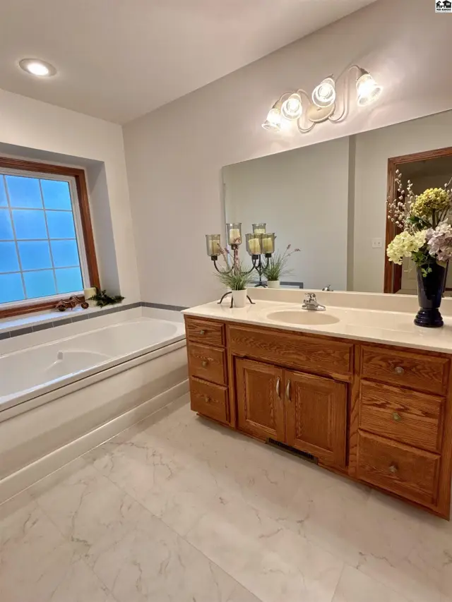 Spacious bathroom features a large soaking tub, double vanity with oak cabinets, and marble tile flooring.