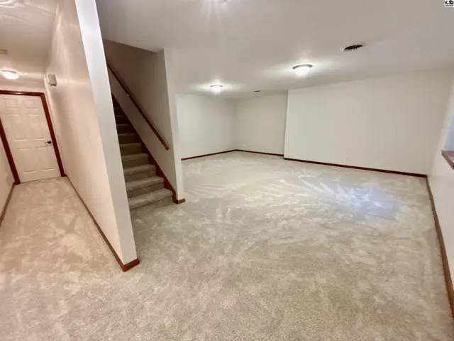 Spacious, unfinished basement with plush carpet, neutral walls, and a carpeted staircase.