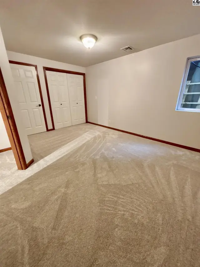 Spacious bedroom with plush beige carpet, white bi-fold closet doors, and a small window.