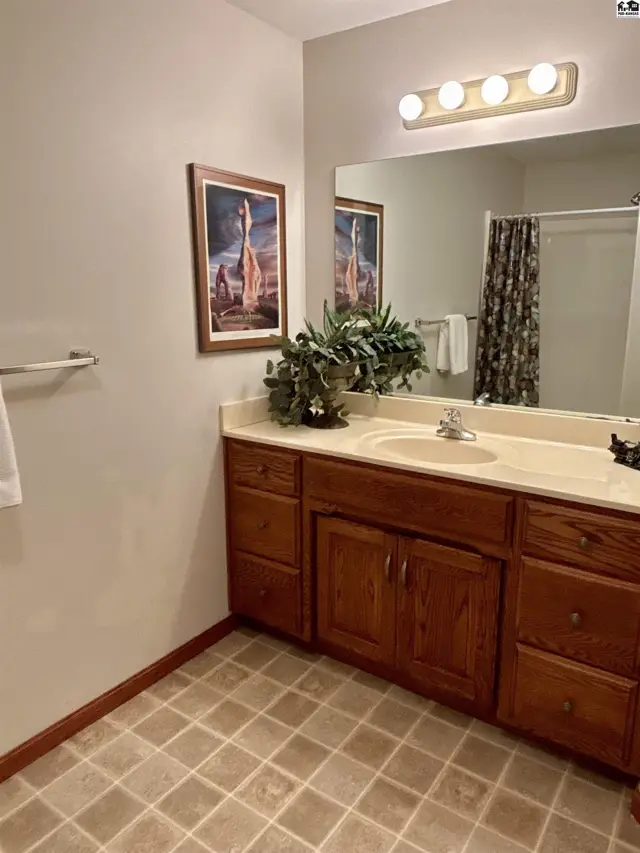 Spacious bathroom with a double vanity, oak cabinets, tiled floor, and a framed artwork.