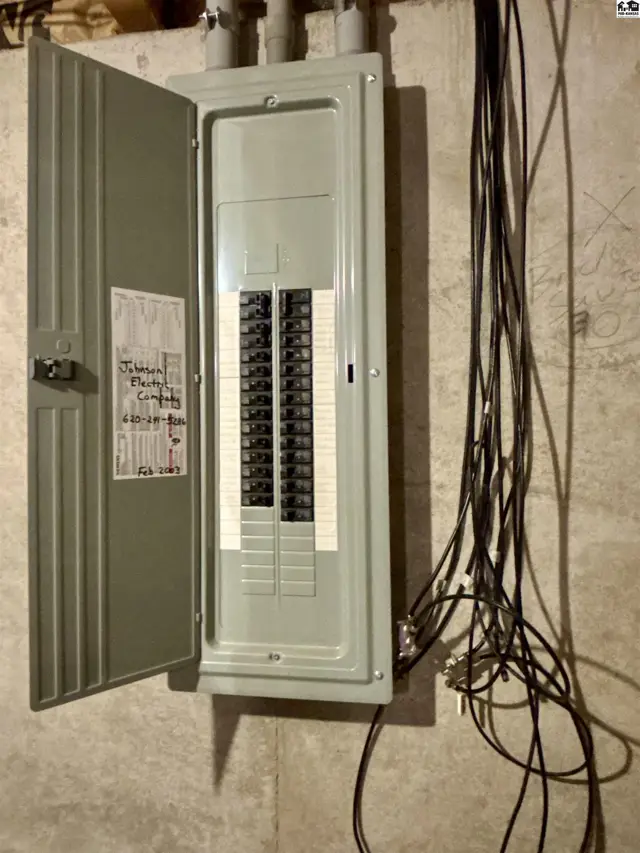 Gray electrical panel with open door and many black wires on a concrete wall.
