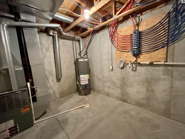 Unfinished basement utility room with concrete walls, furnace, water heater, and plumbing manifold.