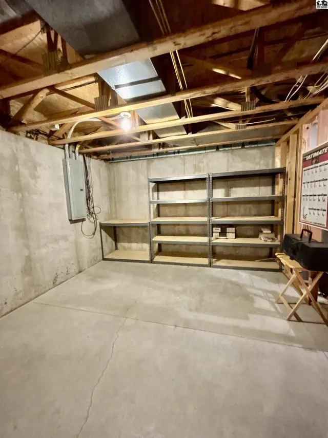 Unfinished basement with concrete walls and floor, exposed joists, and metal shelving.