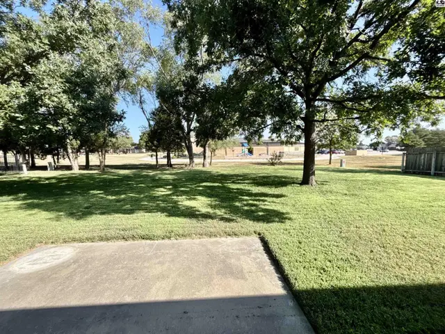 Spacious green lawn with mature trees and a concrete patio area.