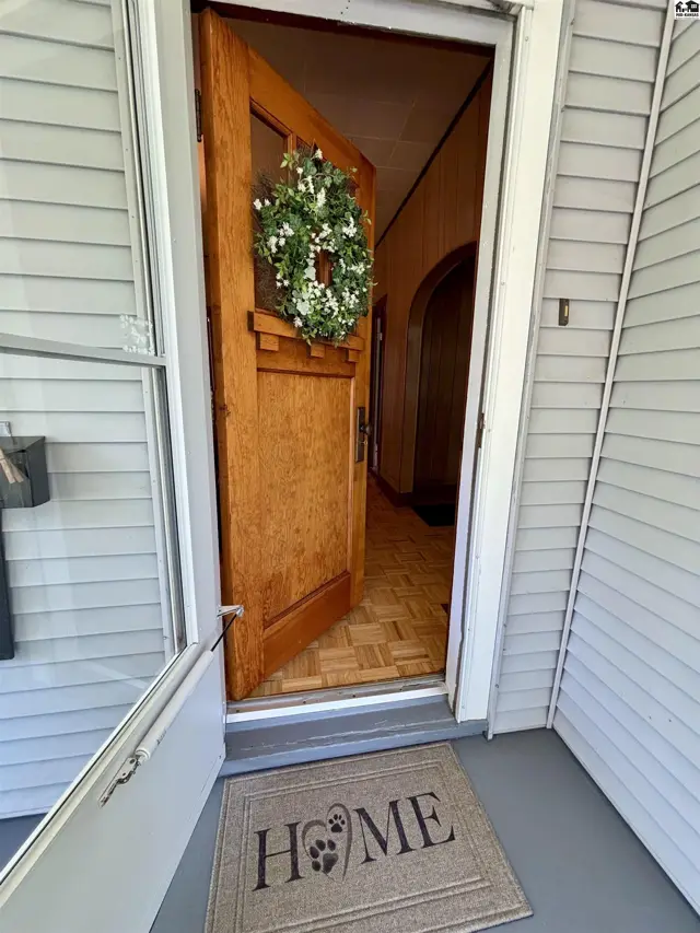 Open wooden front door with wreath reveals entryway with parquet flooring and arched doorway.