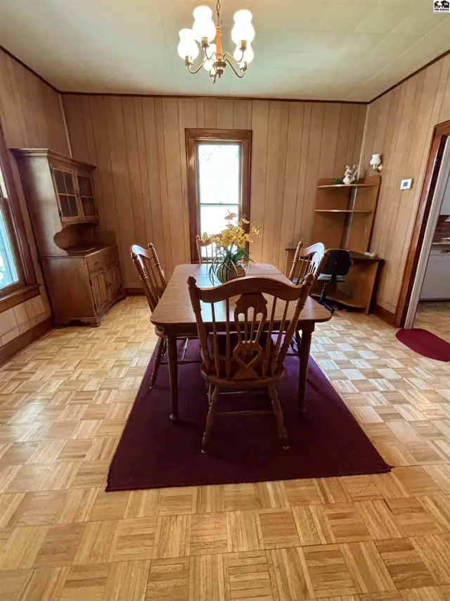 Warm wood-paneled dining room with a table, chairs, hutch, and parquet flooring.