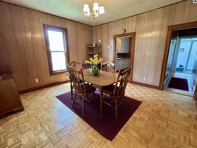 Dining room with wood paneled walls, parquet flooring, and a wooden table with chairs.