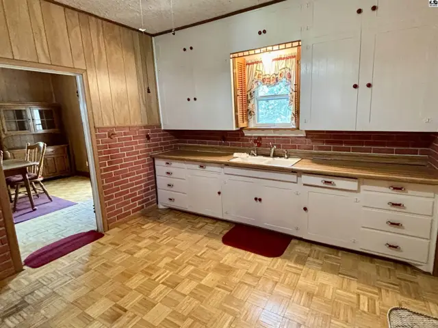 Kitchen with wood-paneled walls, brick backsplash, white cabinets, and parquet flooring.