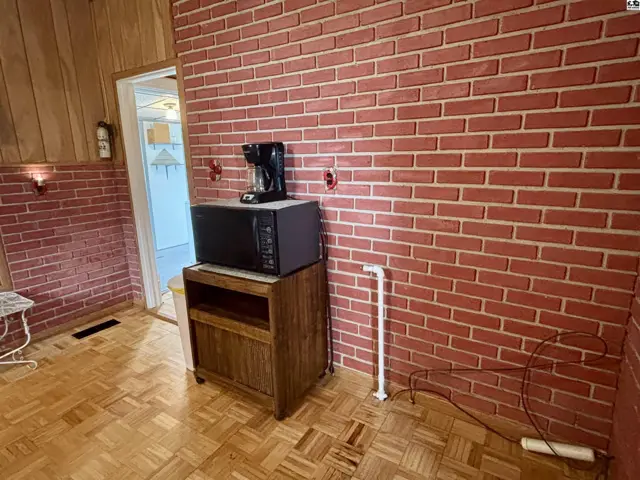 Kitchenette with red brick accent walls, wood cabinetry, parquet flooring, and microwave.