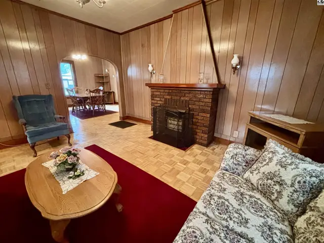 Living room with wood-paneled walls, brick fireplace, parquet flooring, and vintage furnishings.