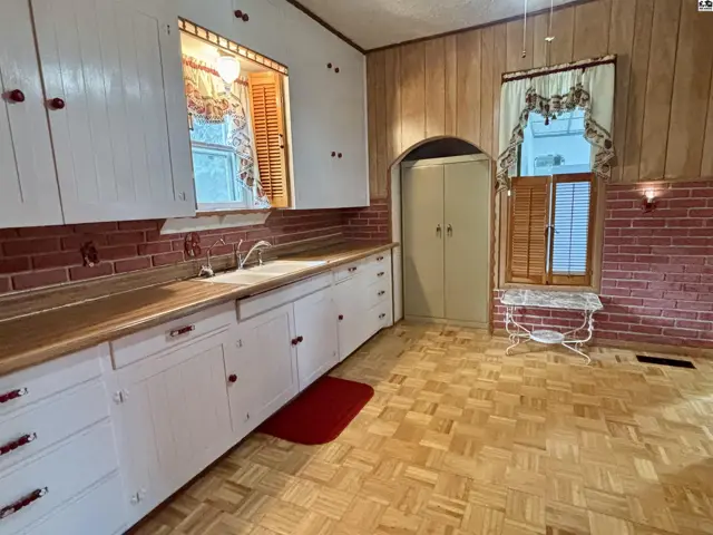 Retro kitchen with white cabinets, wood countertops, brick backsplash, and parquet flooring.