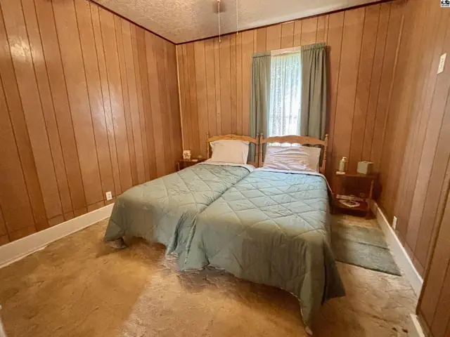 Two twin beds with green quilts sit in a wood-paneled room with a window and light-colored flooring.