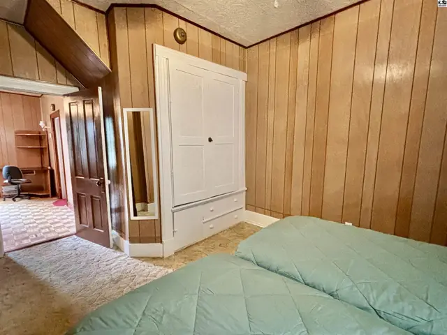Bedroom with wood-paneled walls, a white armoire, and two beds with light green comforters.
