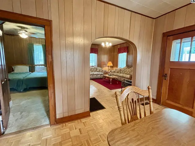 Living room with wood paneled walls, archway to a bedroom, and a dining area with a wooden table.