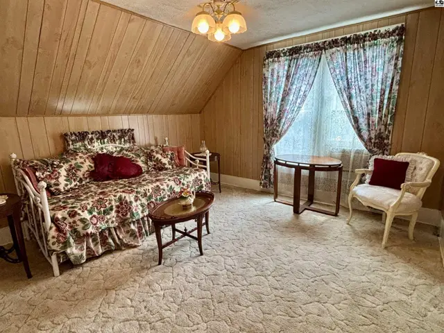 Cozy attic bedroom with wood-paneled walls, floral daybed, and a vintage armchair.
