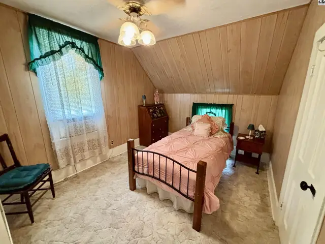 Cozy attic bedroom with wood-paneled walls, a metal-frame bed, and a large window.