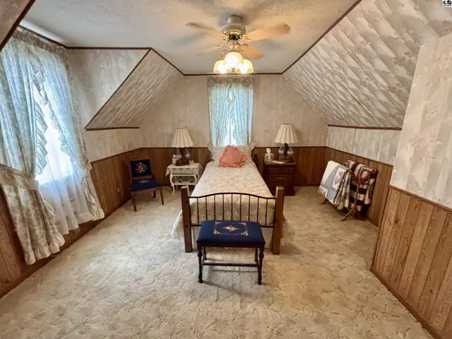 Attic bedroom with sloped ceilings, patterned wallpaper, wood paneling, and a single bed.