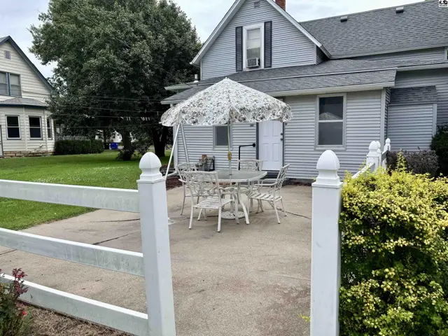 Light blue siding house with a patio, white fence, and outdoor dining set under a floral umbrella.