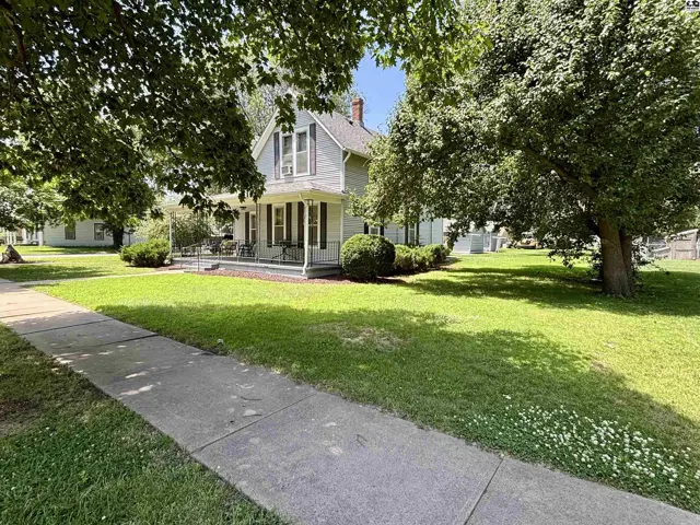 Charming light gray house with a wraparound porch, white trim, and mature trees.