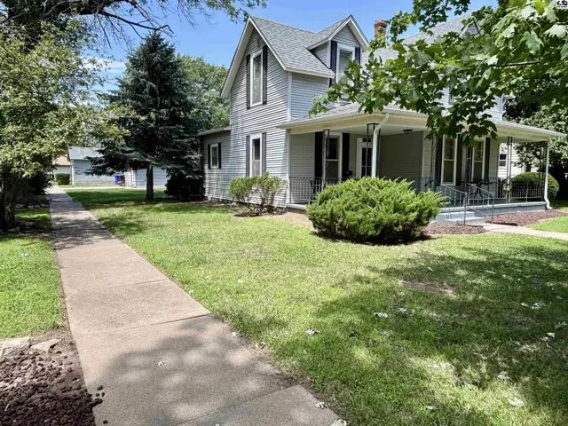 Light gray siding and a wraparound porch highlight this charming two-story home with mature trees.
