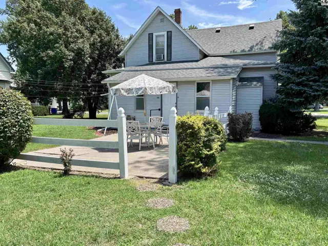 Light blue siding and white picket fence surround a patio with outdoor seating and a swing.