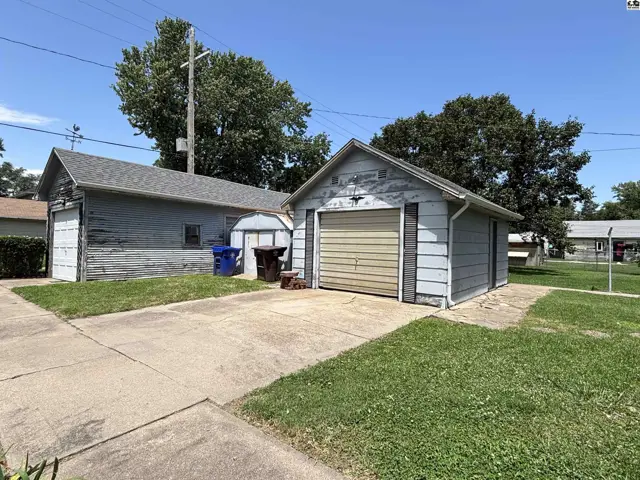 Two detached garages with light blue siding and metal doors sit on a concrete driveway.