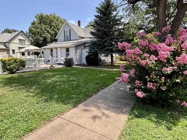 Charming light blue house with white trim, a covered porch, and vibrant pink flowering bushes.