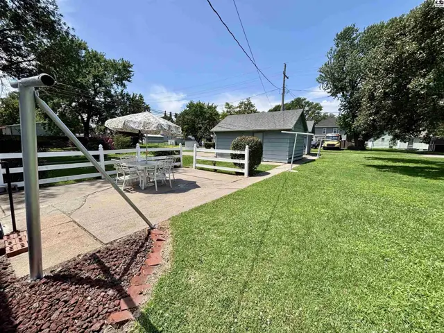 Spacious backyard with a patio, white fence, and detached garage on a sunny day.