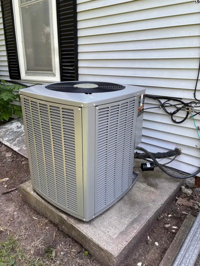Gray outdoor air conditioning unit sits on a concrete pad next to a white-sided house.