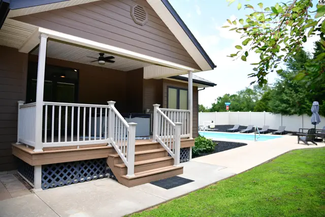 Covered porch with white railings and steps leads to a backyard with a pool and lounge chairs.