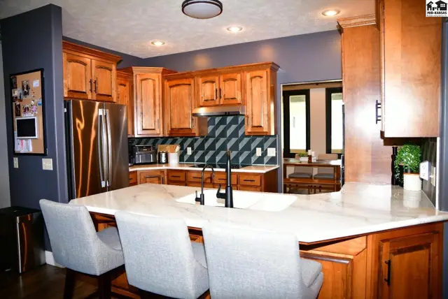 Spacious kitchen with light wood cabinets, granite countertops, stainless steel appliances, and a geometric tile backsplash.