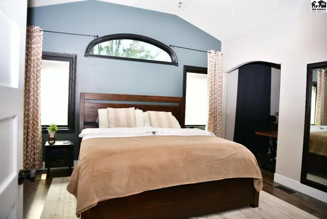 Spacious bedroom with vaulted ceiling, arched window, dark wood furniture, and patterned curtains.