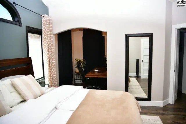 Spacious bedroom with a vaulted ceiling, arched window, and an adjoining den viewed through an archway.