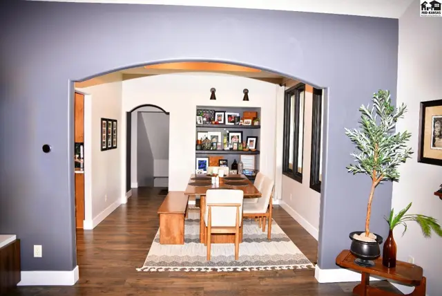 Arched entryway reveals a dining room with wood floors, built-in shelves, and modern furnishings.