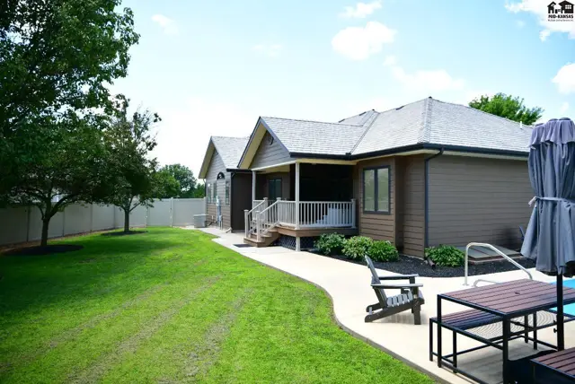 Exterior view of a brown-sided home with a covered porch, white railings, and a swimming pool.