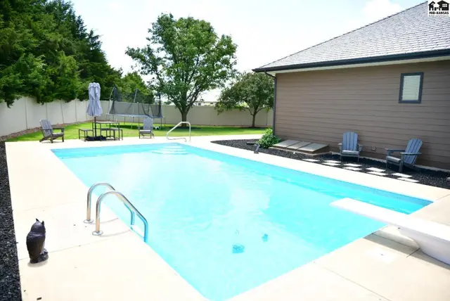 Spacious backyard features a bright blue swimming pool, patio, and trampoline.